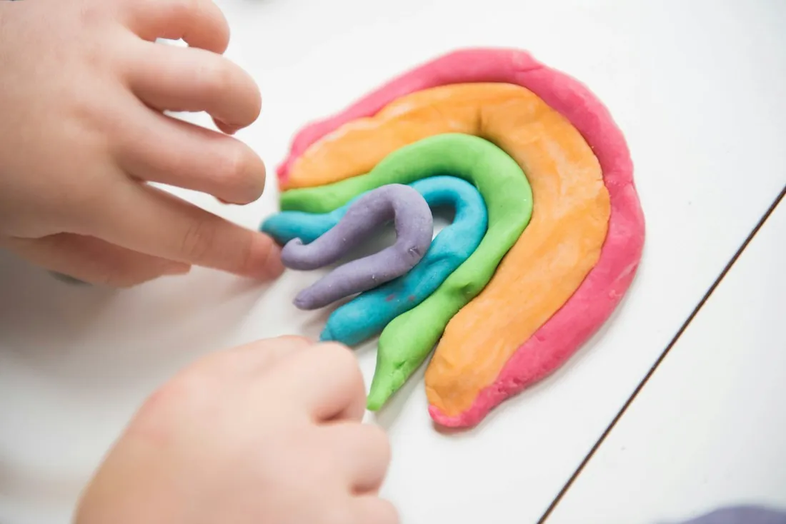 Small hands shaping a rainbow out of soft modeling dough.