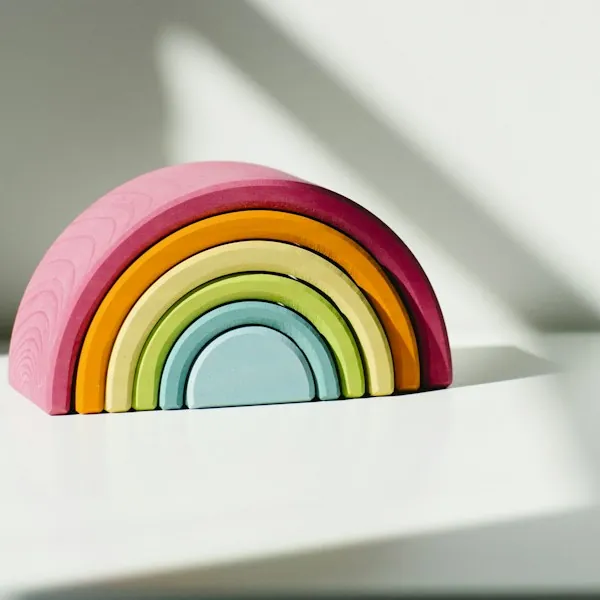 A pastel wooden rainbow stacking toy on a sunlit white shelf.